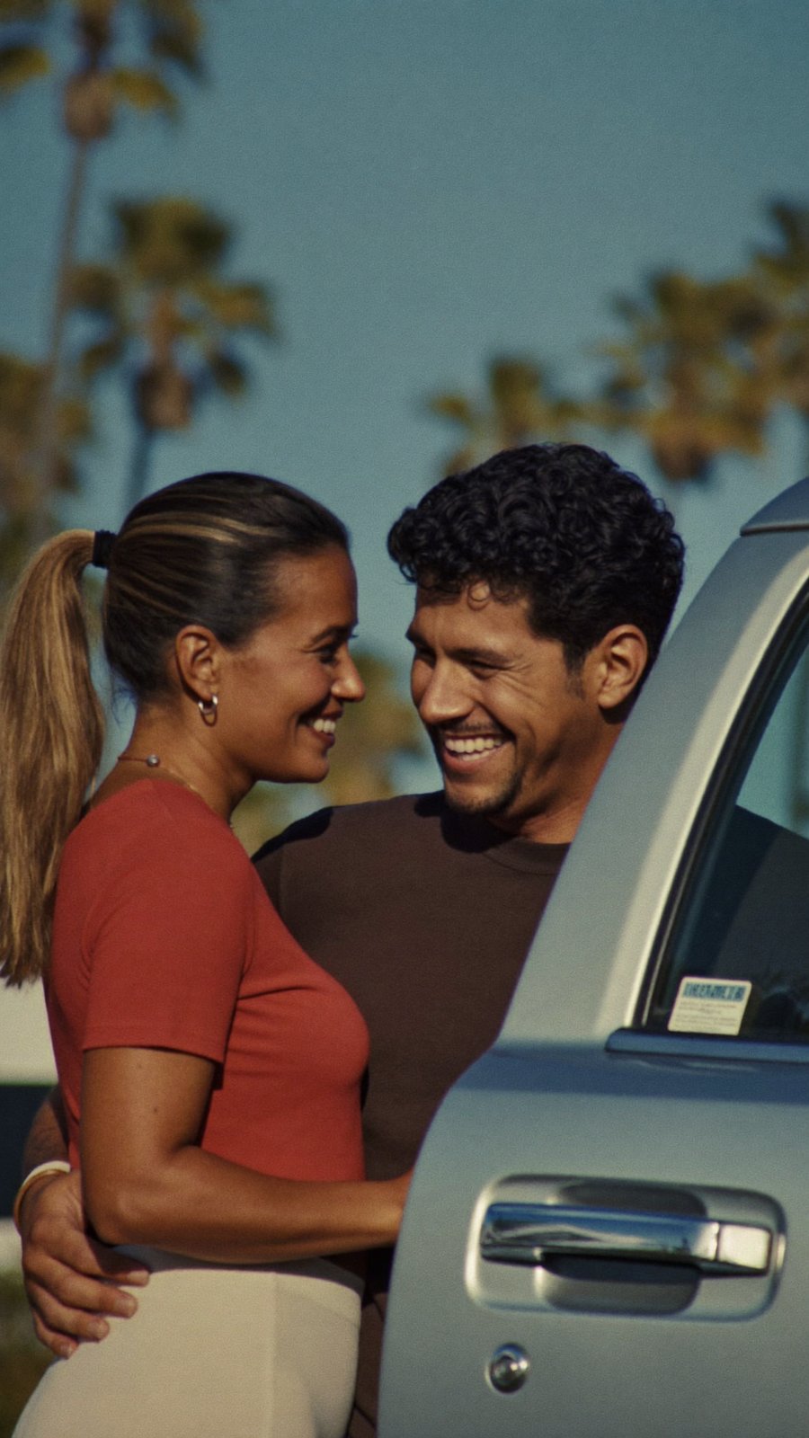 A couple laughing beside the open door of their new truck